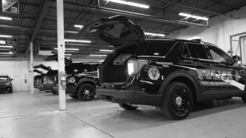 black-and-white image of police emergency vehicles with open trunks inside parking garage